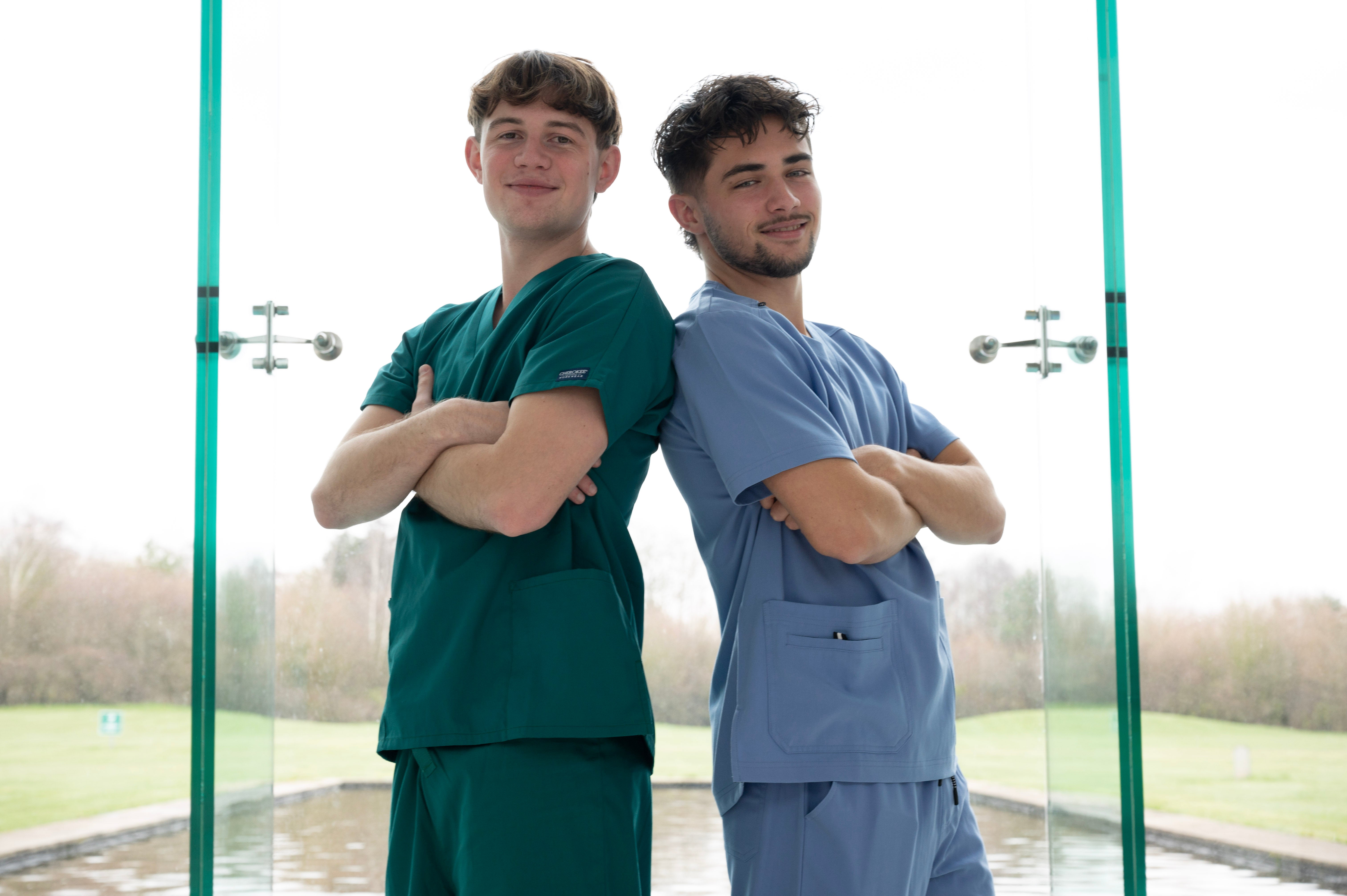 Deux aides-soignants dos à dos en tenues vert forêt et bleu ciel.